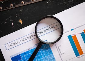 Close-up of a magnifying glass over financial data charts and metrics on printed paper.